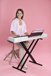 Photo of Smiling woman playing synthesizer on pink background