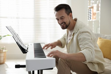 Photo of Smiling man playing synthesizer at home. Electronic musical instrument