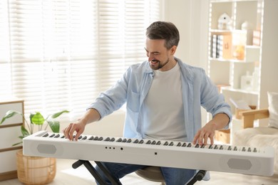 Photo of Smiling man playing synthesizer at home. Electronic musical instrument