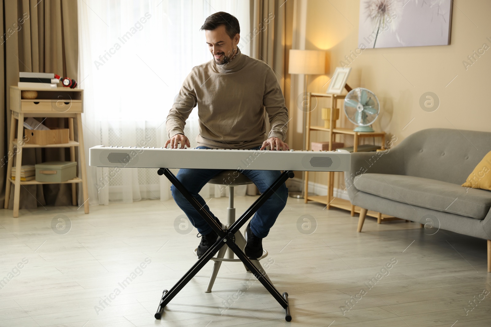 Photo of Smiling man playing synthesizer at home. Electronic musical instrument