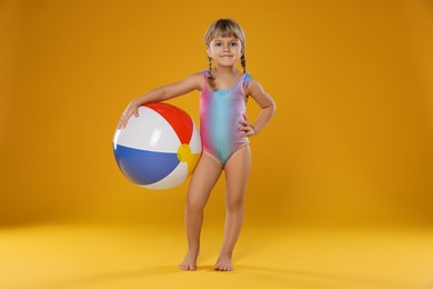 Photo of Cute little girl in swimsuit with inflatable ball on orange background