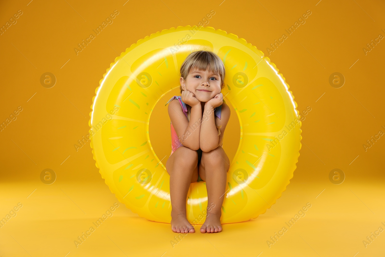 Photo of Cute little girl in swimsuit with inflatable ring and on orange background