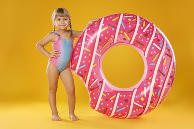 Photo of Cute little girl in swimsuit with inflatable ring on orange background