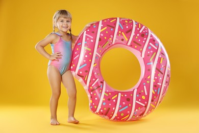 Photo of Cute little girl in swimsuit with inflatable ring on orange background