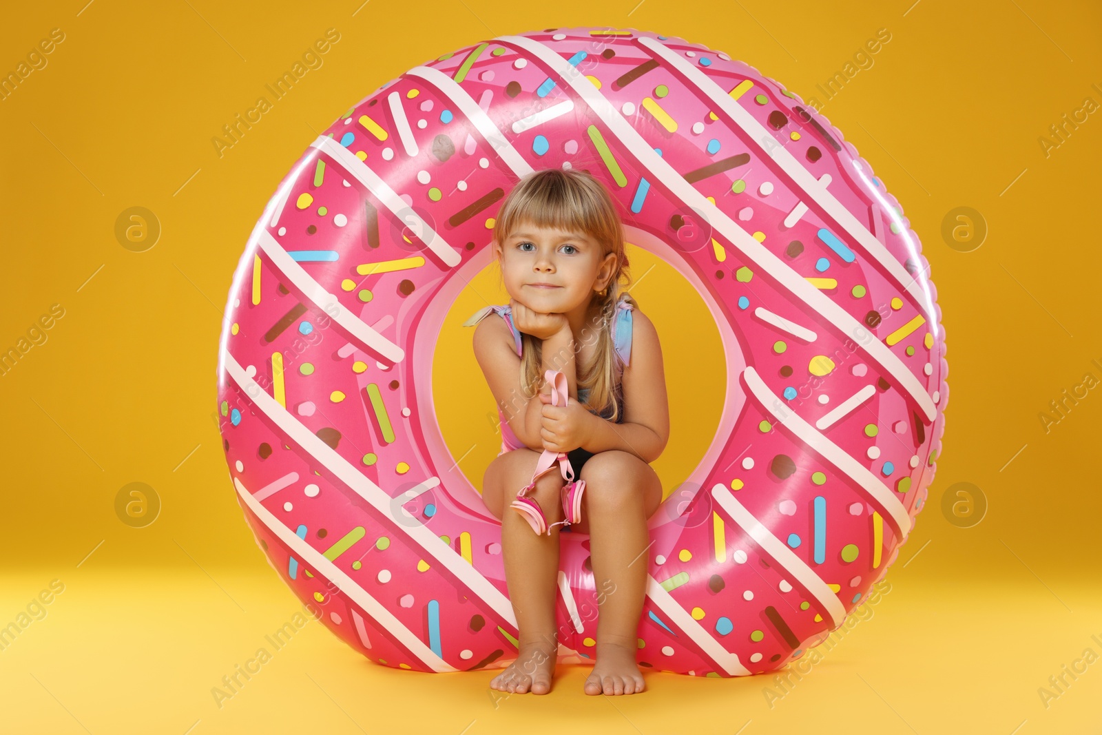 Photo of Cute little girl in swimsuit with inflatable ring and on orange background