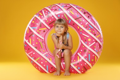 Photo of Cute little girl in swimsuit with inflatable ring and on orange background