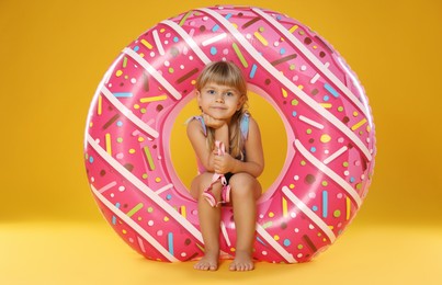 Photo of Cute little girl in swimsuit with inflatable ring and on orange background