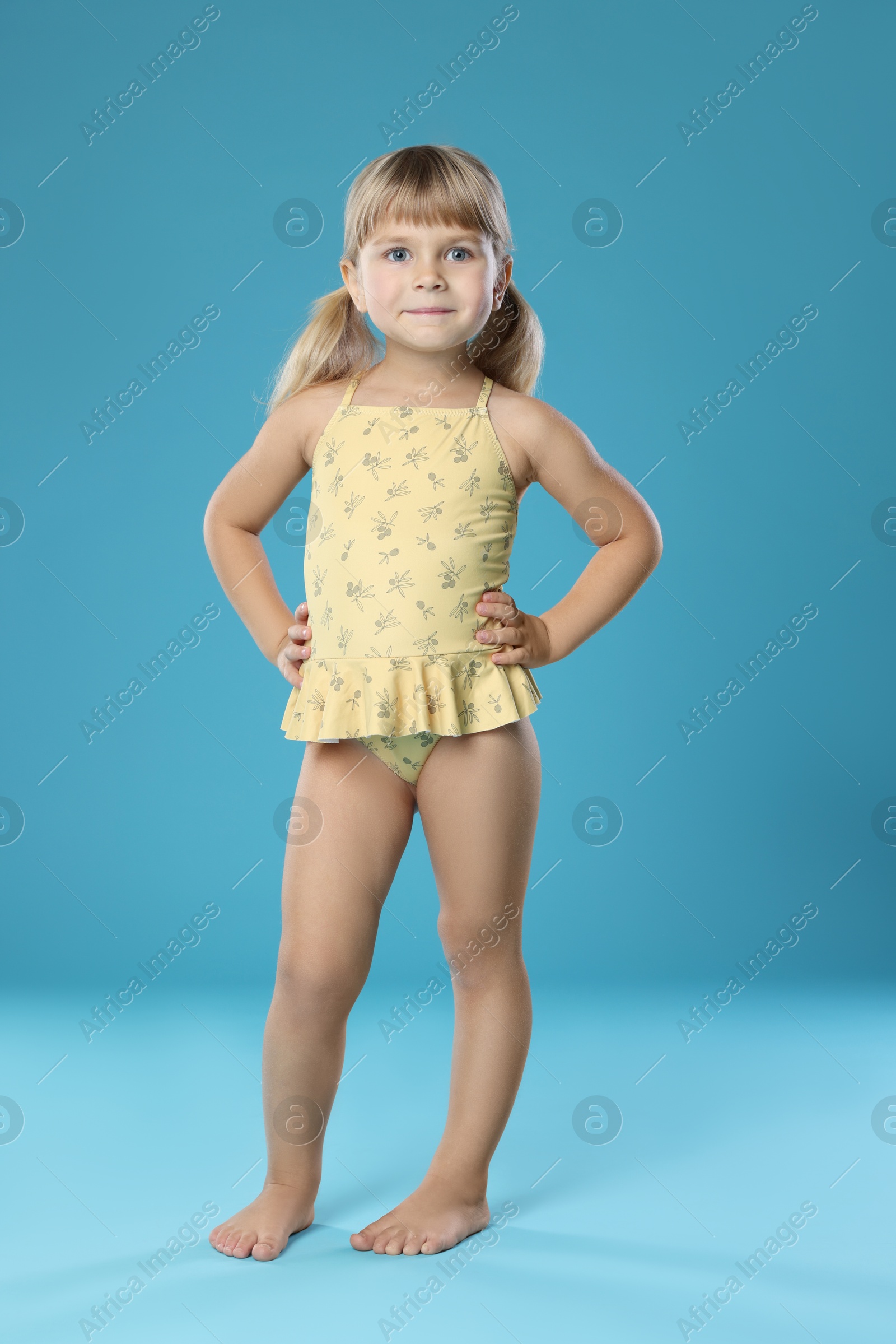 Photo of Cute little girl in swimsuit on light blue background