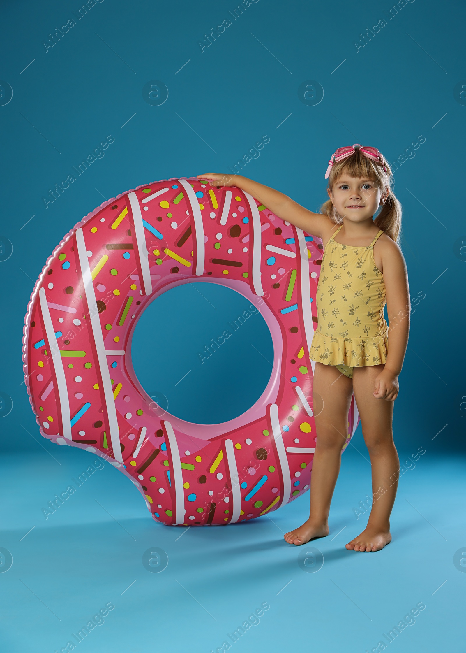 Photo of Cute little girl in swimsuit with inflatable ring and swim goggles on light blue background