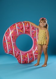 Photo of Cute little girl in swimsuit with inflatable ring and swim goggles on light blue background