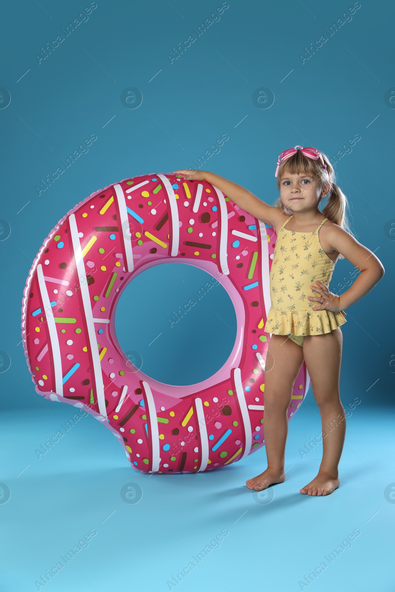 Photo of Cute little girl in swimsuit with inflatable ring and swim goggles on light blue background