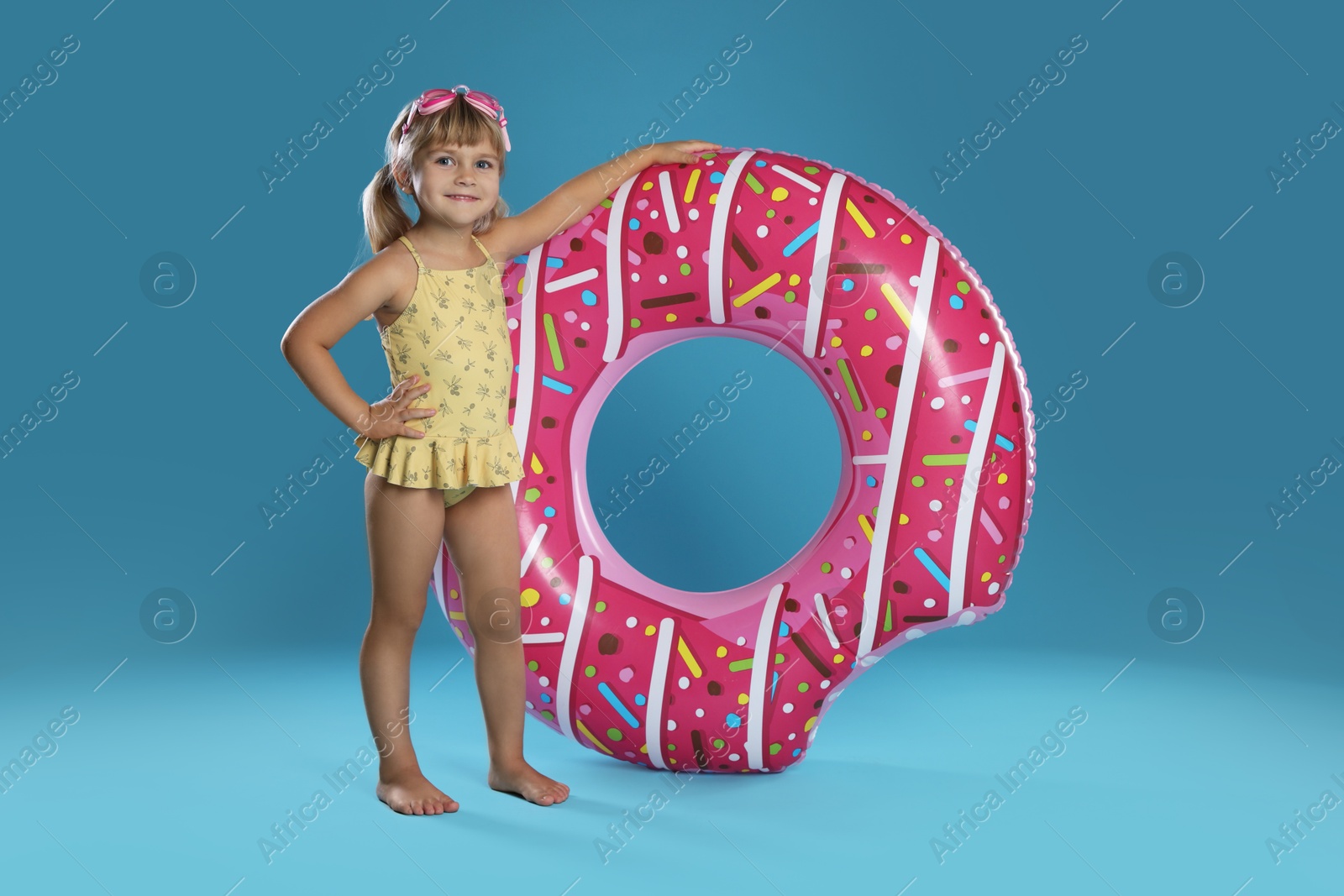 Photo of Cute little girl in swimsuit with inflatable ring and swim goggles on light blue background