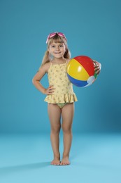 Photo of Cute little girl in swimsuit with inflatable ball and swim goggles on light blue background