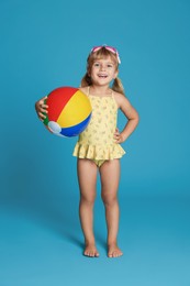 Photo of Cute little girl in swimsuit with inflatable ball and swim goggles on light blue background