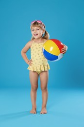 Photo of Cute little girl in swimsuit with inflatable ball and swim goggles on light blue background