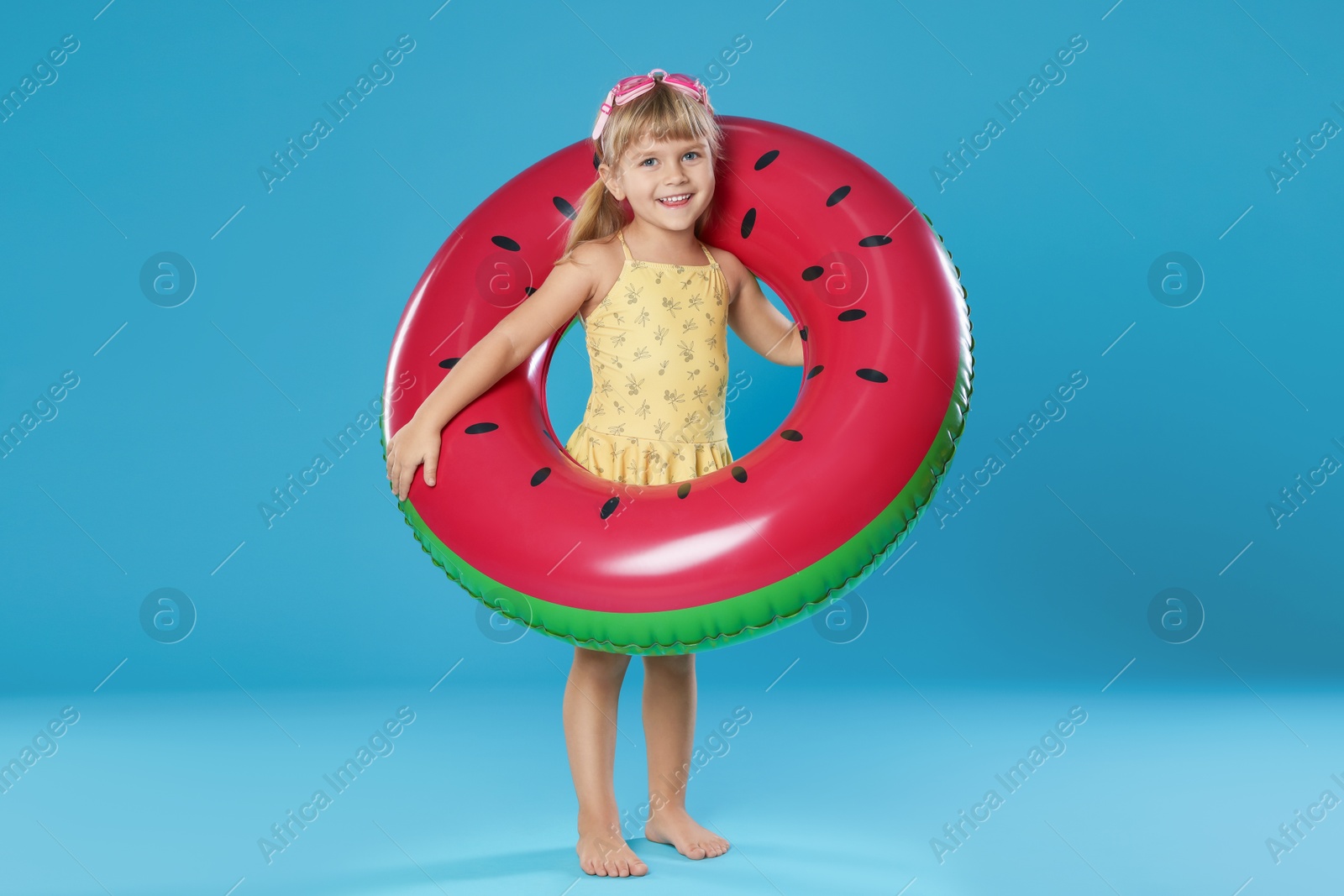 Photo of Cute little girl in swimsuit with inflatable ring and swim goggles on light blue background