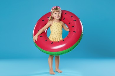 Photo of Cute little girl in swimsuit with inflatable ring and swim goggles on light blue background