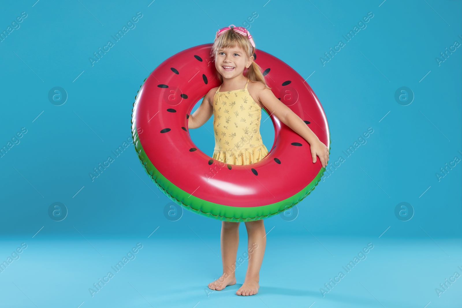 Photo of Cute little girl in swimsuit with inflatable ring and swim goggles on light blue background