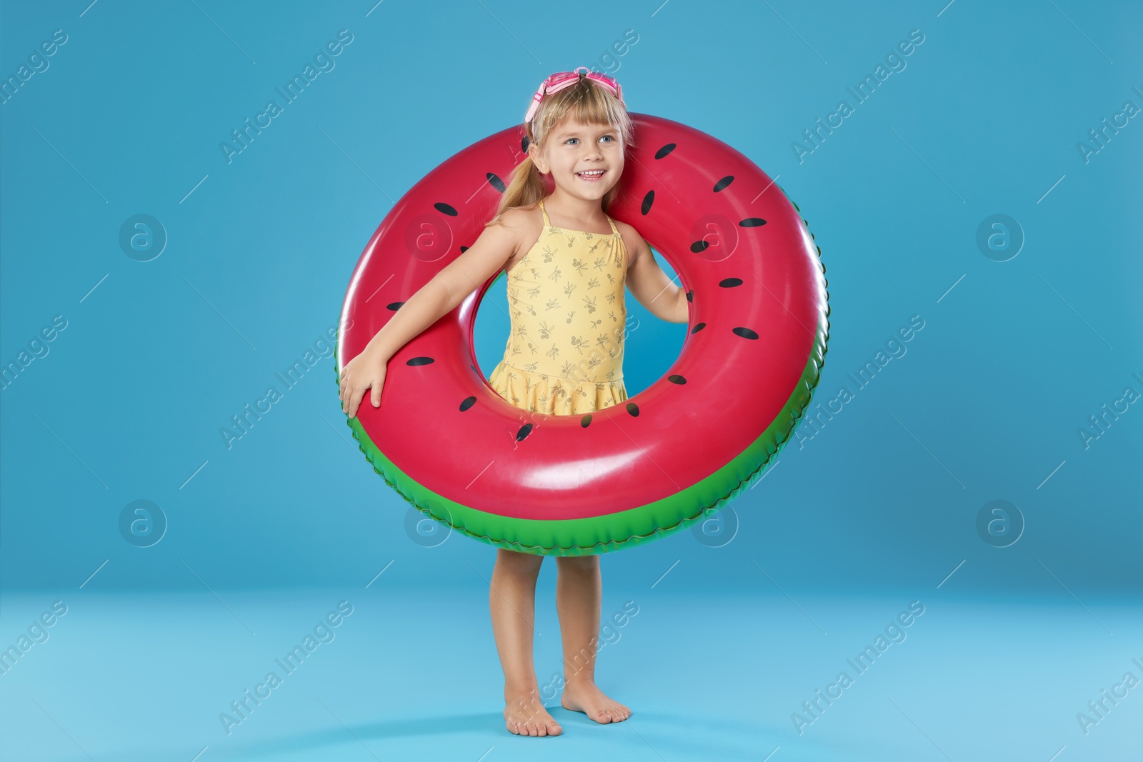 Photo of Cute little girl in swimsuit with inflatable ring and swim goggles on light blue background