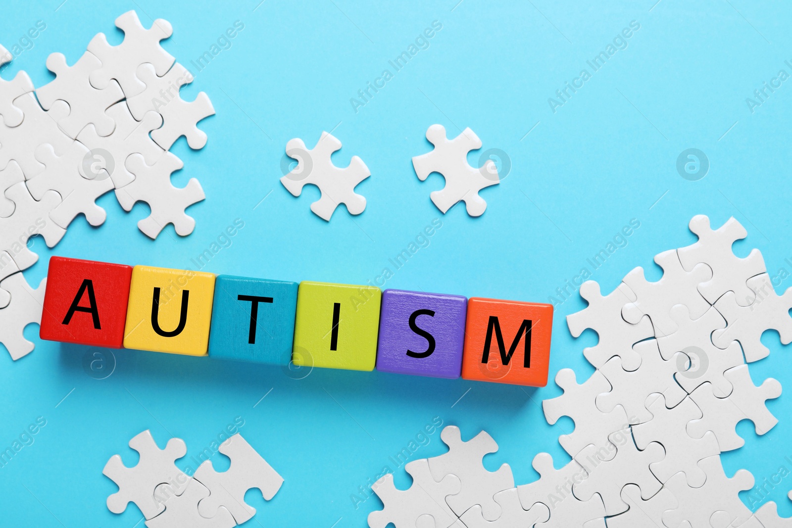 Photo of Word Autism made of colorful cubes and puzzle on light blue background, flat lay