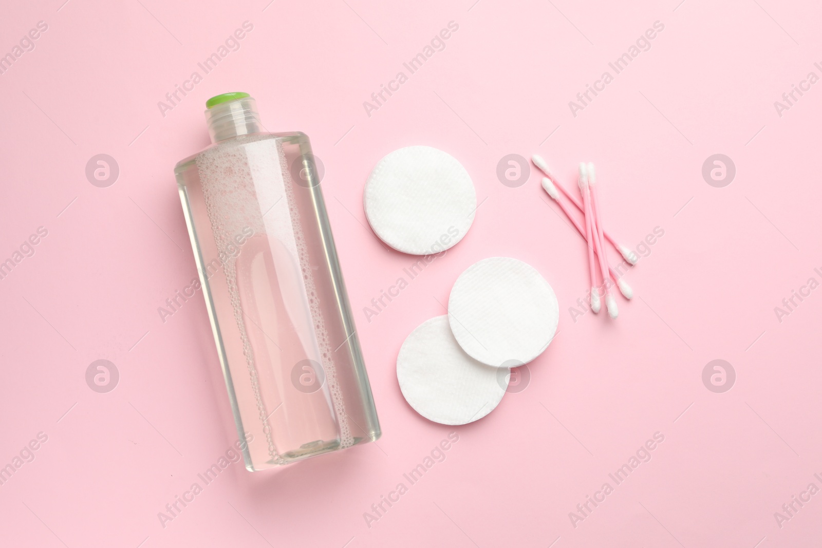 Photo of Cotton pads, swabs and bottle of cosmetic product on pink background, flat lay