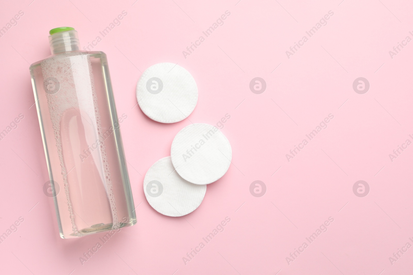 Photo of Cotton pads and bottle of cosmetic product on pink background, flat lay. Space for text