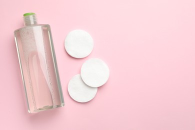 Photo of Cotton pads and bottle of cosmetic product on pink background, flat lay. Space for text