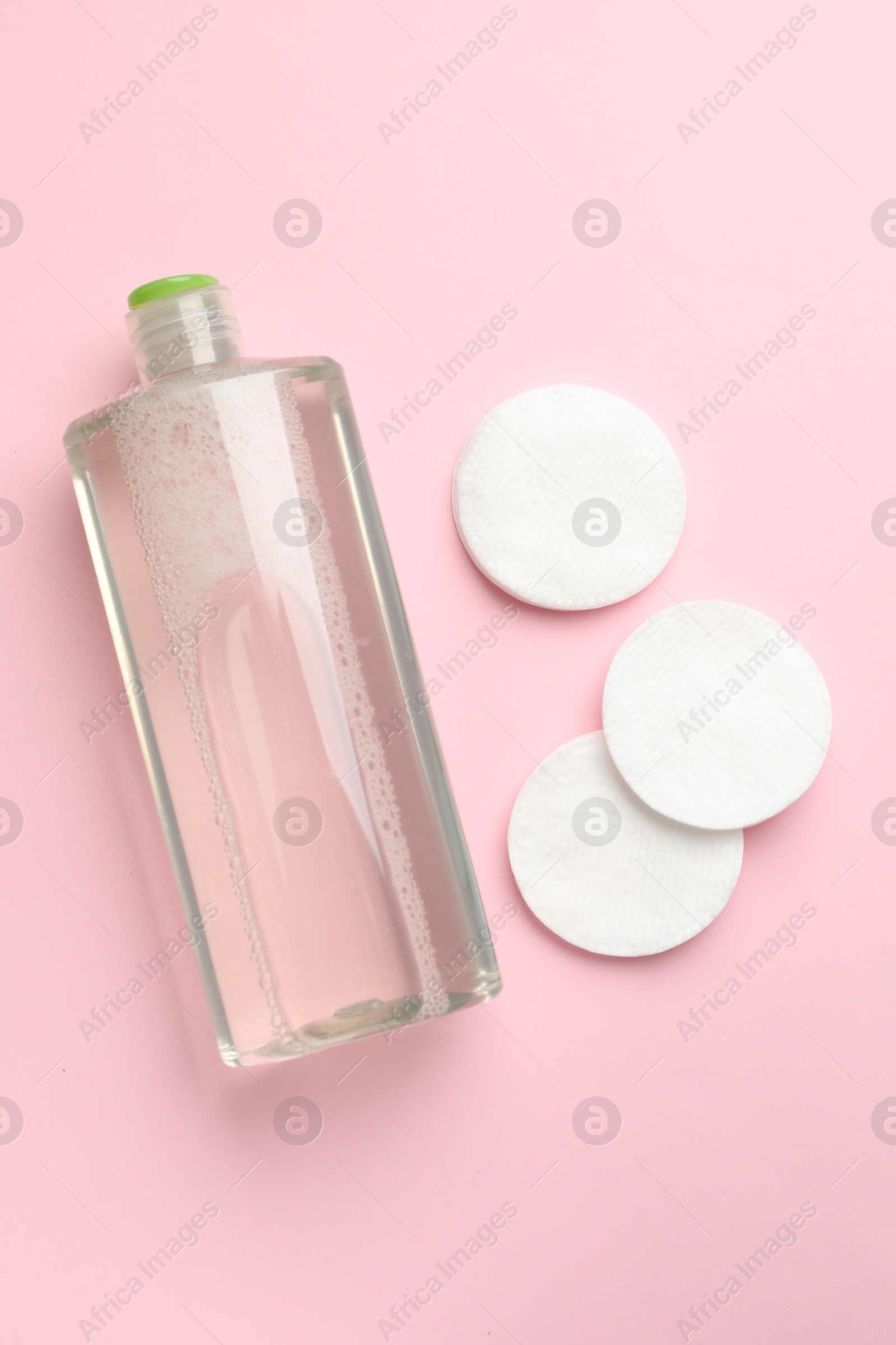 Photo of Cotton pads and bottle of cosmetic product on pink background, flat lay