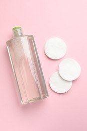 Photo of Cotton pads and bottle of cosmetic product on pink background, flat lay