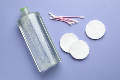 Photo of Cotton pads, swabs and bottle of cosmetic product on violet background, flat lay