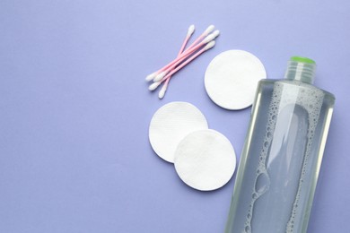 Photo of Cotton pads, swabs and bottle of cosmetic product on violet background, flat lay. Space for text