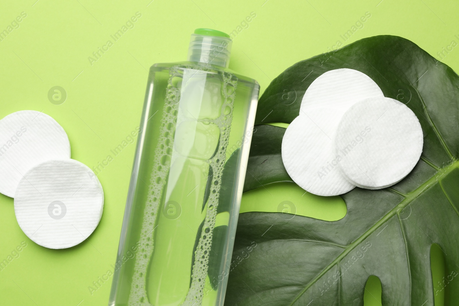 Photo of Cotton pads, cosmetic product and monstera leaf on green background, flat lay