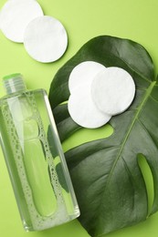 Photo of Cotton pads, cosmetic product and monstera leaf on green background, flat lay