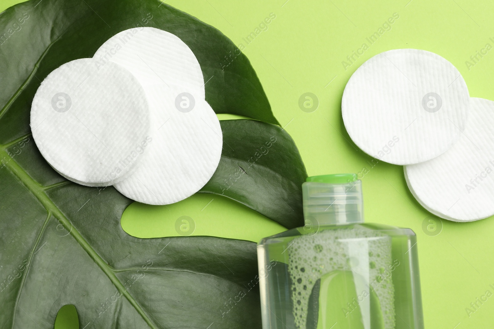 Photo of Cotton pads, cosmetic product and monstera leaf on green background, flat lay