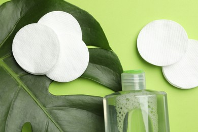 Photo of Cotton pads, cosmetic product and monstera leaf on green background, flat lay