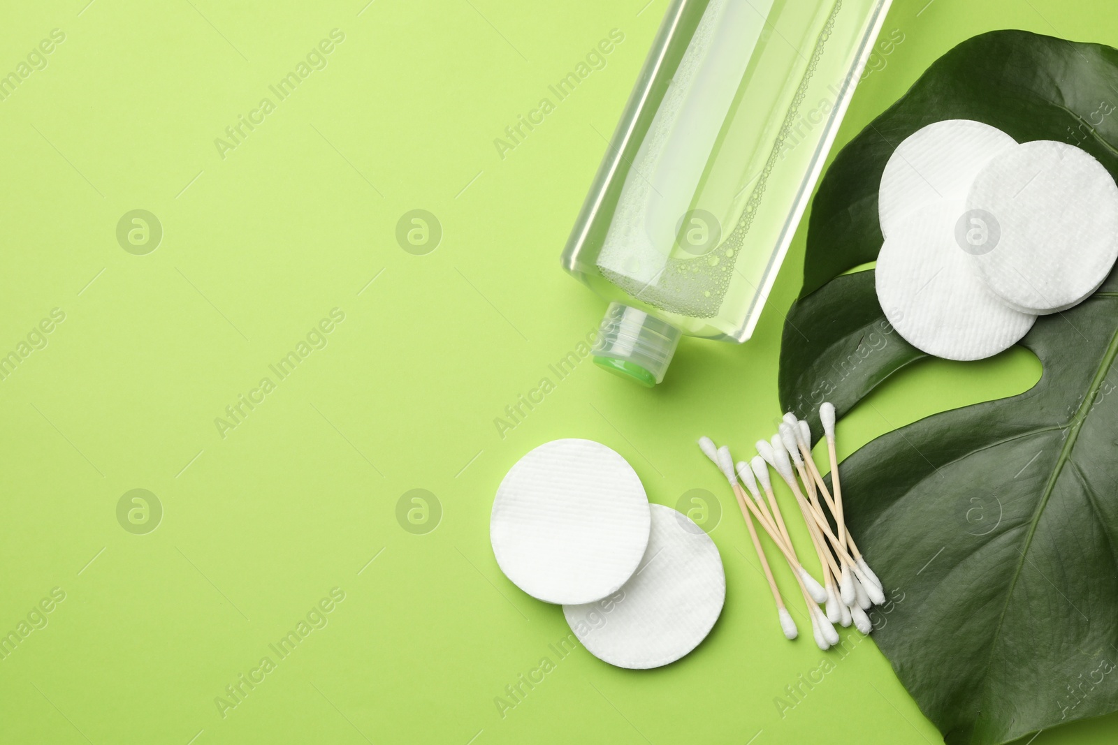 Photo of Cotton pads, swabs, cosmetic product and monstera leaf on green background, flat lay. Space for text