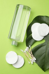 Photo of Cotton pads, swabs, cosmetic product and monstera leaf on green background, flat lay