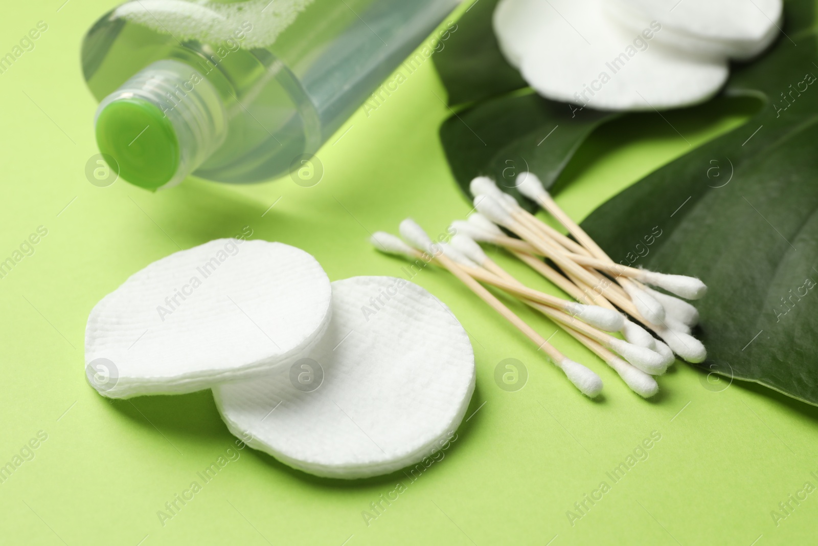 Photo of Cotton pads, swabs, cosmetic product and monstera leaf on green background, closeup