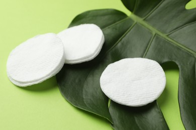 Photo of Cotton pads and monstera leaf on green background, closeup