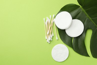 Photo of Cotton pads, swabs and monstera leaf on green background, flat lay. Space for text