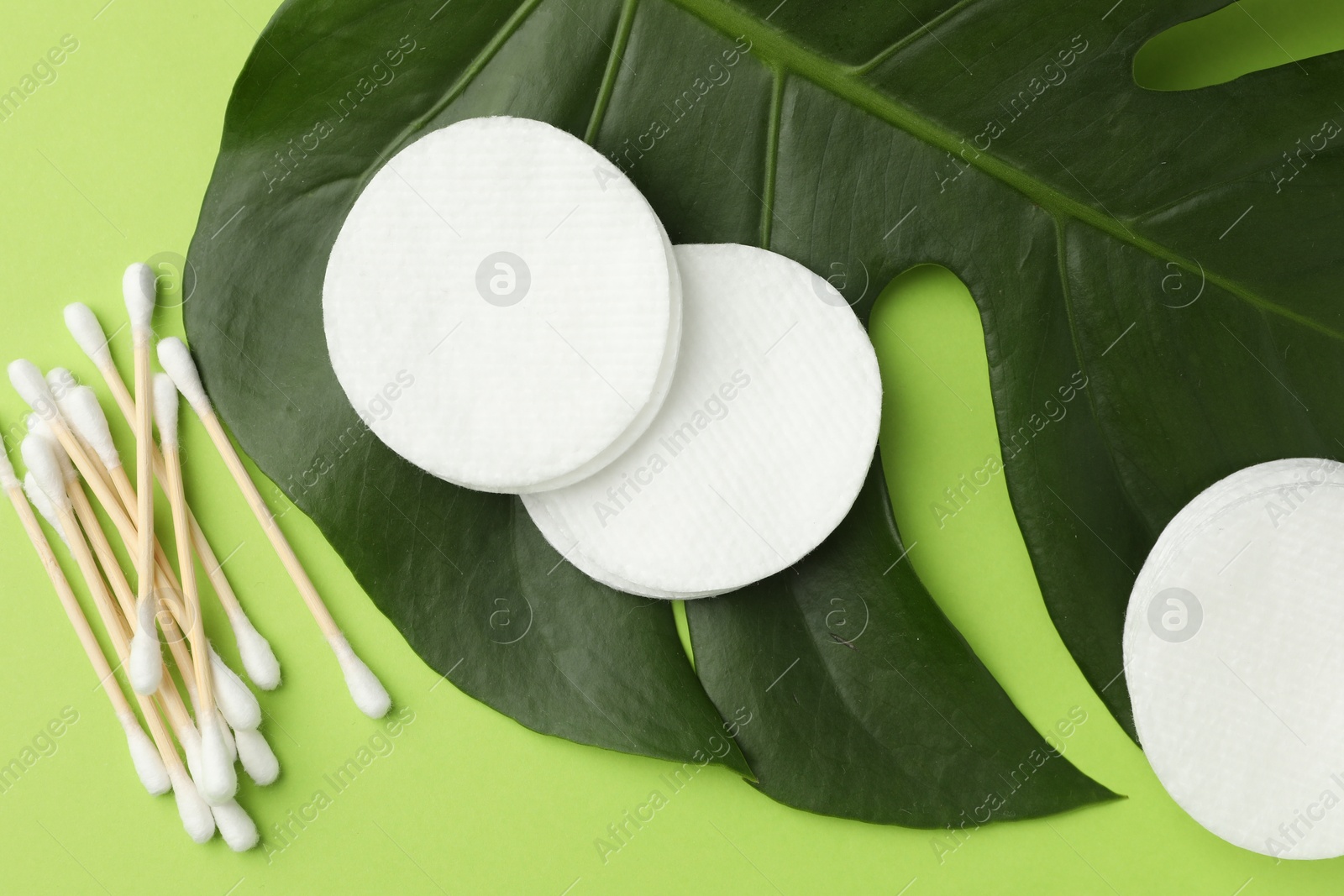 Photo of Cotton pads, swabs and monstera leaf on green background, flat lay