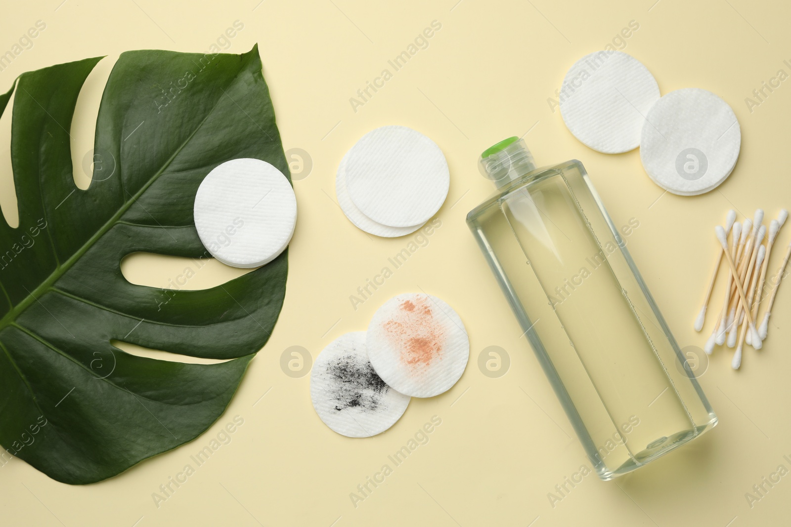 Photo of Cotton pads, swabs, bottle of makeup remover and monstera leaf on beige background, flat lay