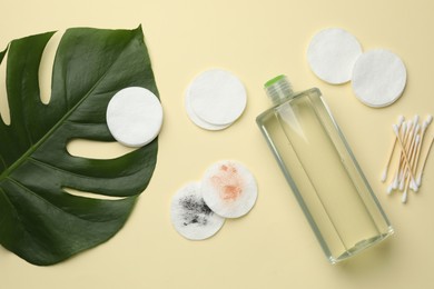 Photo of Cotton pads, swabs, bottle of makeup remover and monstera leaf on beige background, flat lay