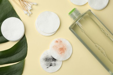 Photo of Cotton pads, swabs, bottle of makeup remover and monstera leaf on beige background, flat lay