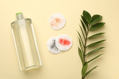 Photo of Dirty cotton pads, bottle of makeup remover and green branch on beige background, flat lay