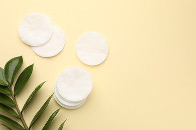 Photo of Cotton pads and green branch on beige background, flat lay. Space for text