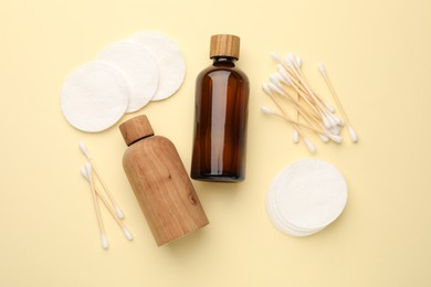 Photo of Cotton pads, bottles of cosmetic products and swabs on beige background, flat lay