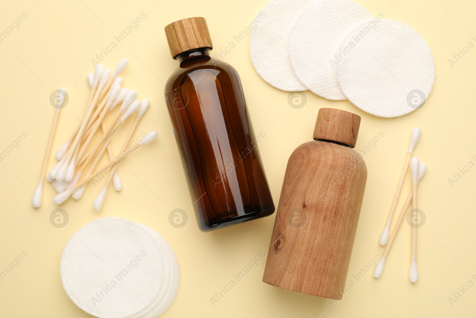 Photo of Cotton pads, bottles of cosmetic products and swabs on beige background, flat lay