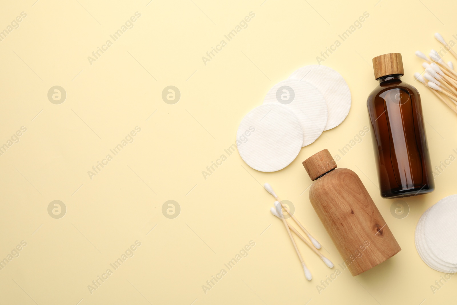 Photo of Cotton pads, bottles of cosmetic products and swabs on beige background, flat lay. Space for text