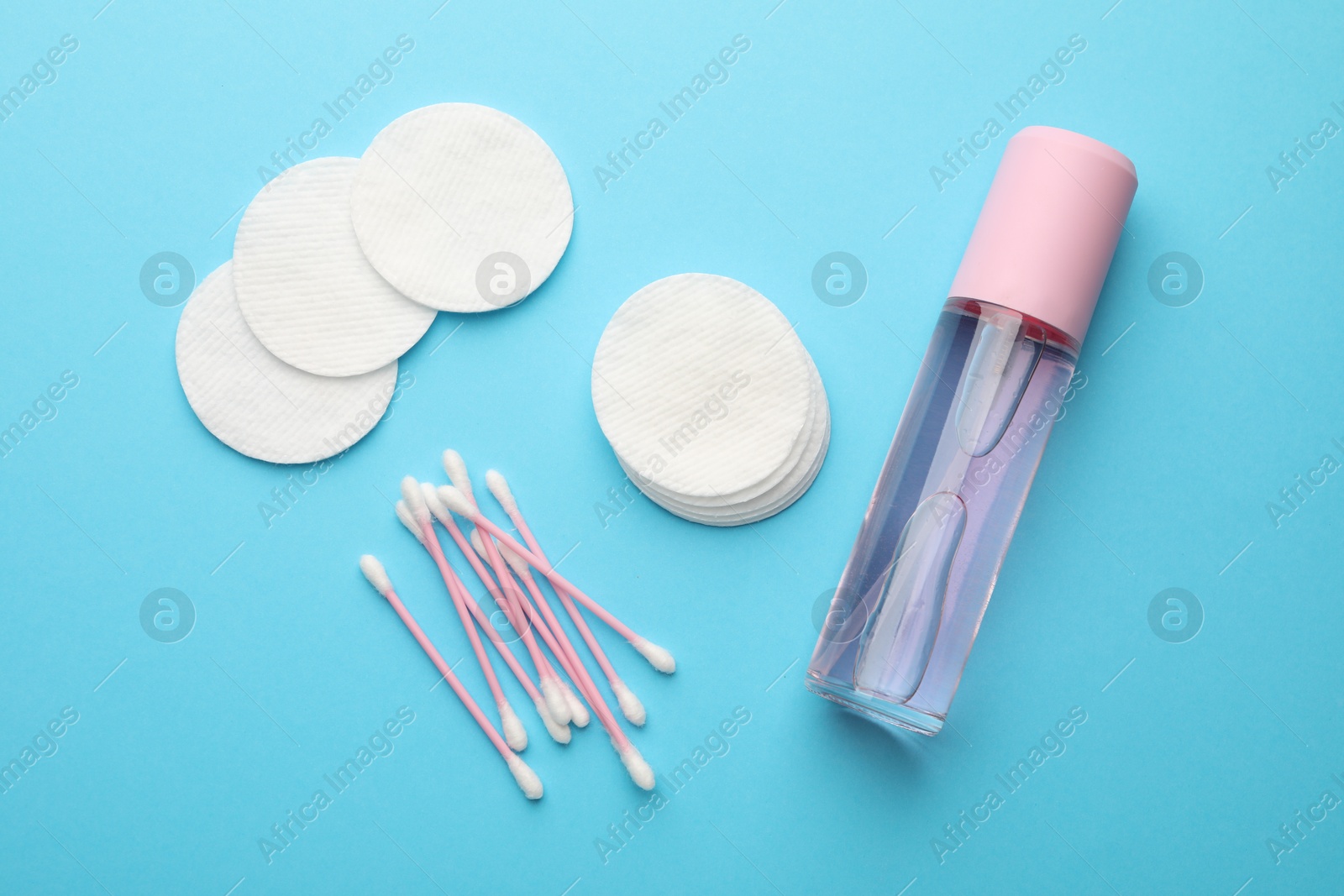 Photo of Cotton pads, bottle of cosmetic product and swabs on light blue background, flat lay